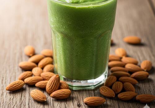 Smoothie vert servi dans un verre avec amandes autour